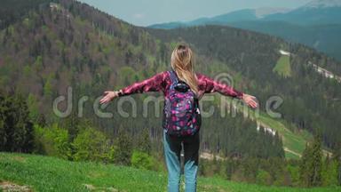 一个年轻的高加索女人带着背包和太阳镜站在山顶上举起双手。 概念